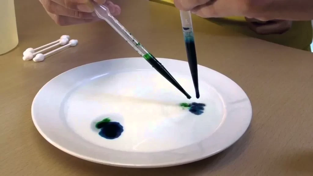 Pipetter drypper farve på en skål mælk