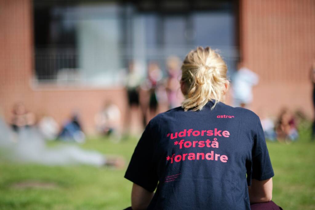 Elev sidder med ryggen til - på T-shirten står der UDFORSKE FORSTÅ FORANDRE