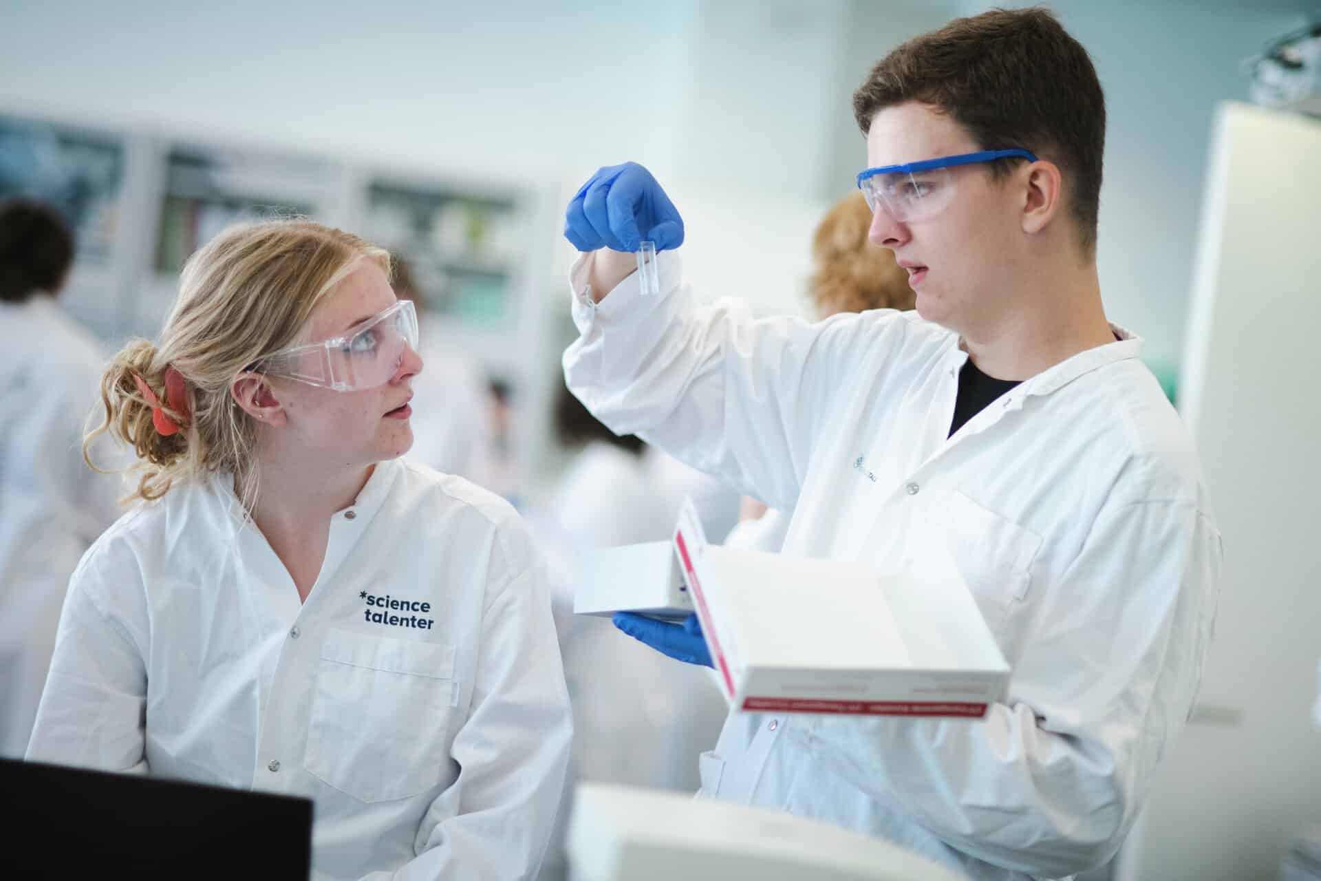 Elever i laboratoriekitler og med briller kigger på udstyr
