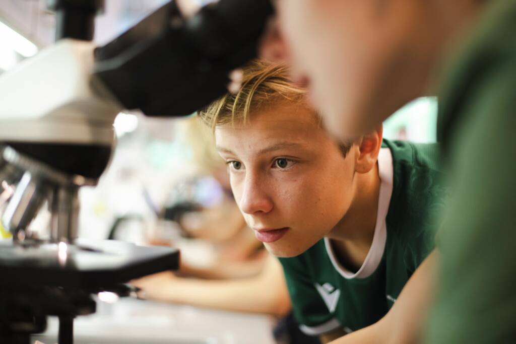 Elev kigger interesseret med mens hans kammerat kigger i mikroskop